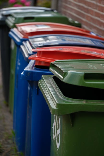 A collection of discarded rubbish situated on an outdoor paved surface, consisting of black garbage bags, a yellow plastic container, and a pair of old, weathered car tires leaning against a rough sto