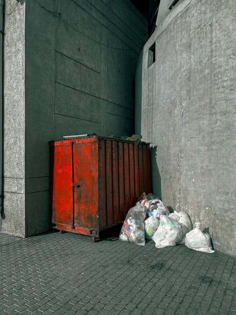 Close-up view of a light grey wall with black, three-dimensional text reading 'trash here' positioned on the left side. To the right of the text, a black downward arrow symbol indicates the location f